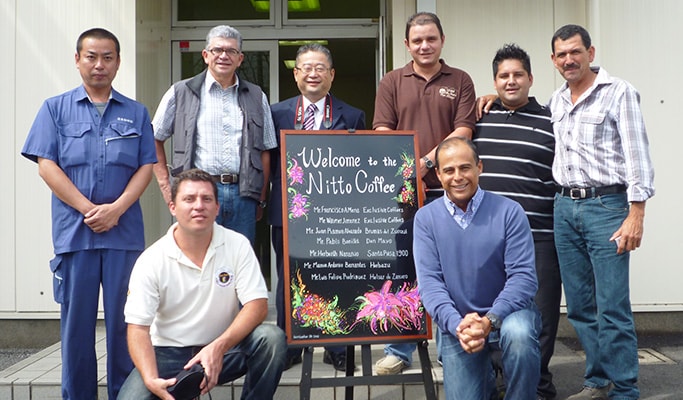 「Welcome to the Nitto Coffee」と書かれた立て看板の周りを社長や創業者、従業員と囲んで撮った集合写真